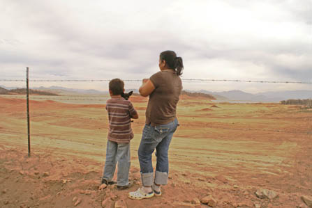 Foto de un niño y su madre, mirando a través de un campo vacío hacia la minera en la distancia.